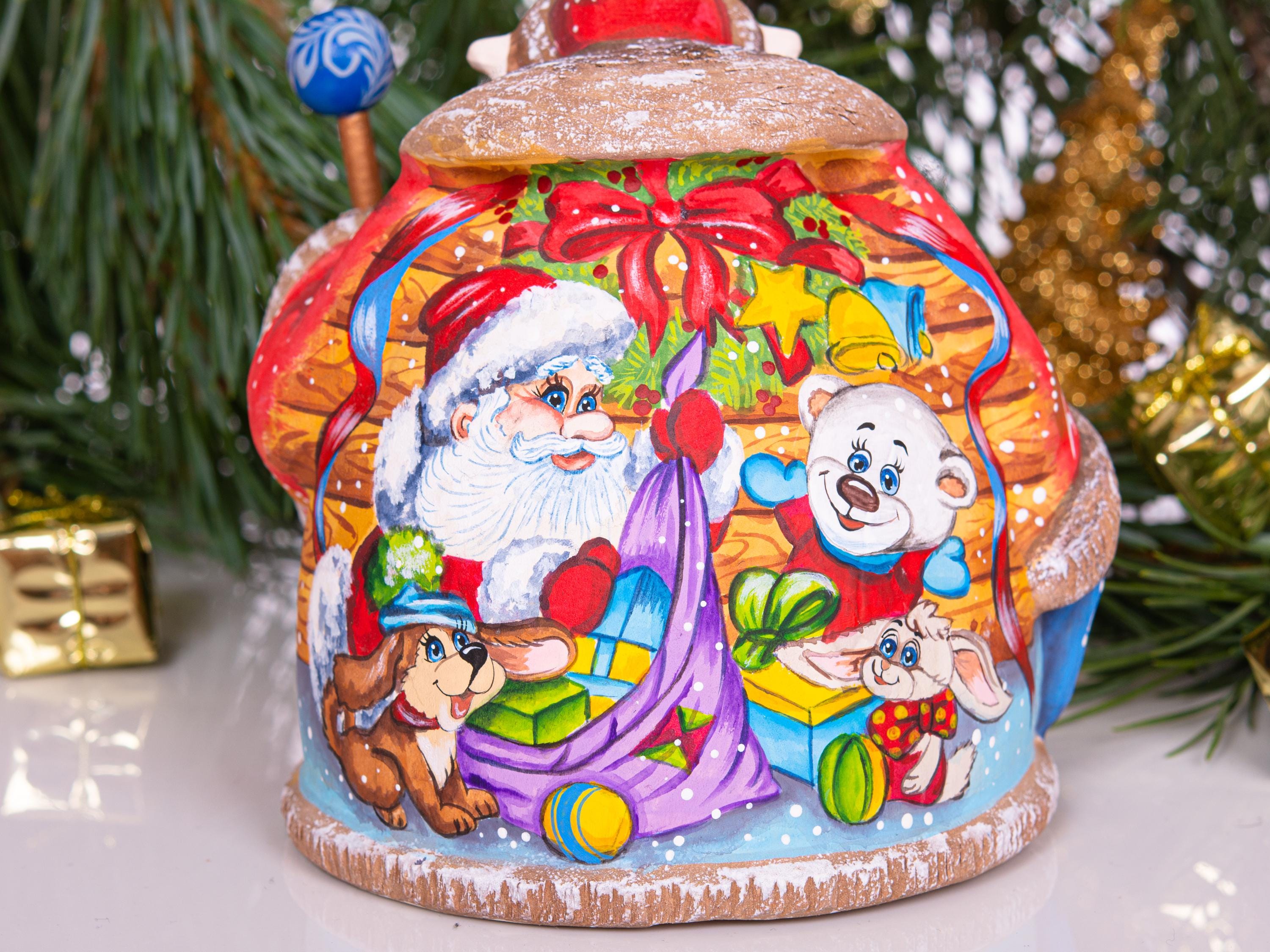 A hand-painted ceramic Christmas ornament shaped like a house, featuring Santa Claus, a white bear, a dachshund, and a rabbit carrying gifts, set against a festive holiday background with pine branches and gold ornaments.